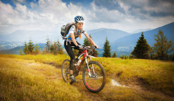 Картинка спорт велоспорт деревья пейзаж футболка велосипед горы очки грязь рюкзак кроссовки лосины косички шлем перчатки облака девушка трава