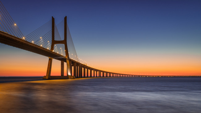 Обои картинки фото города, - мосты, река, тахо, тежу, лиссабон, португалия, закат, оранжевый, вечер, небо, синее, освещение, фонари, васко, да, гама, мост