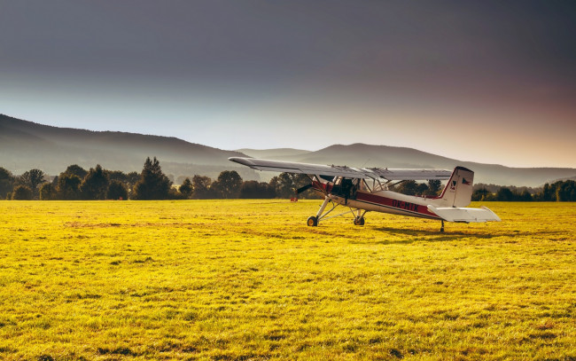 Обои картинки фото авиация, лёгкие одномоторные самолёты, поле, самолет, трава, лес, дымка, солнечно, горы