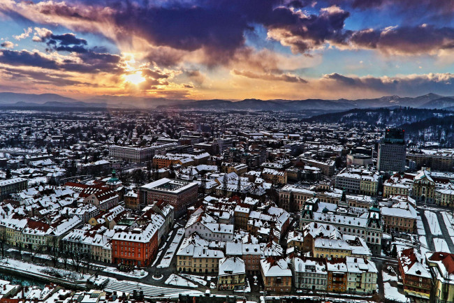 Обои картинки фото города, - панорамы, панорама, город, крыши, небо, тучи, солнце, горы, снег