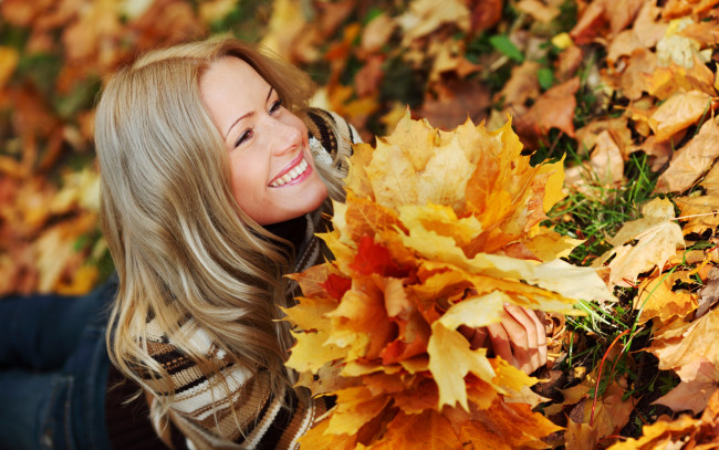 Обои картинки фото девушки, -unsort , лица,  портреты, лежит, взгляд, блондинка, улыбка, листья, девушка, джинсы, свитер, трава, осень